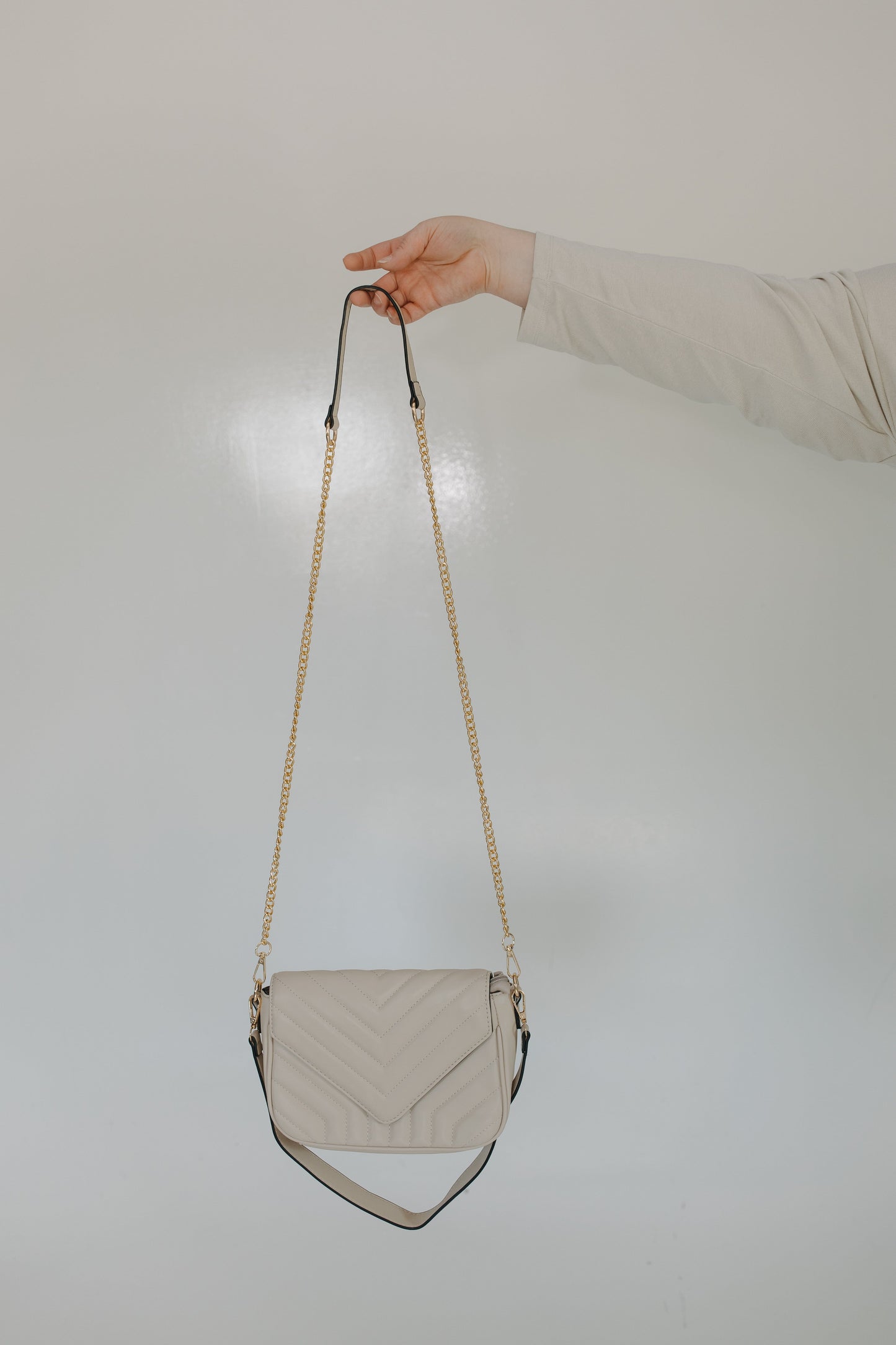 Beige handbag with a chain strap held by a hand against a light background