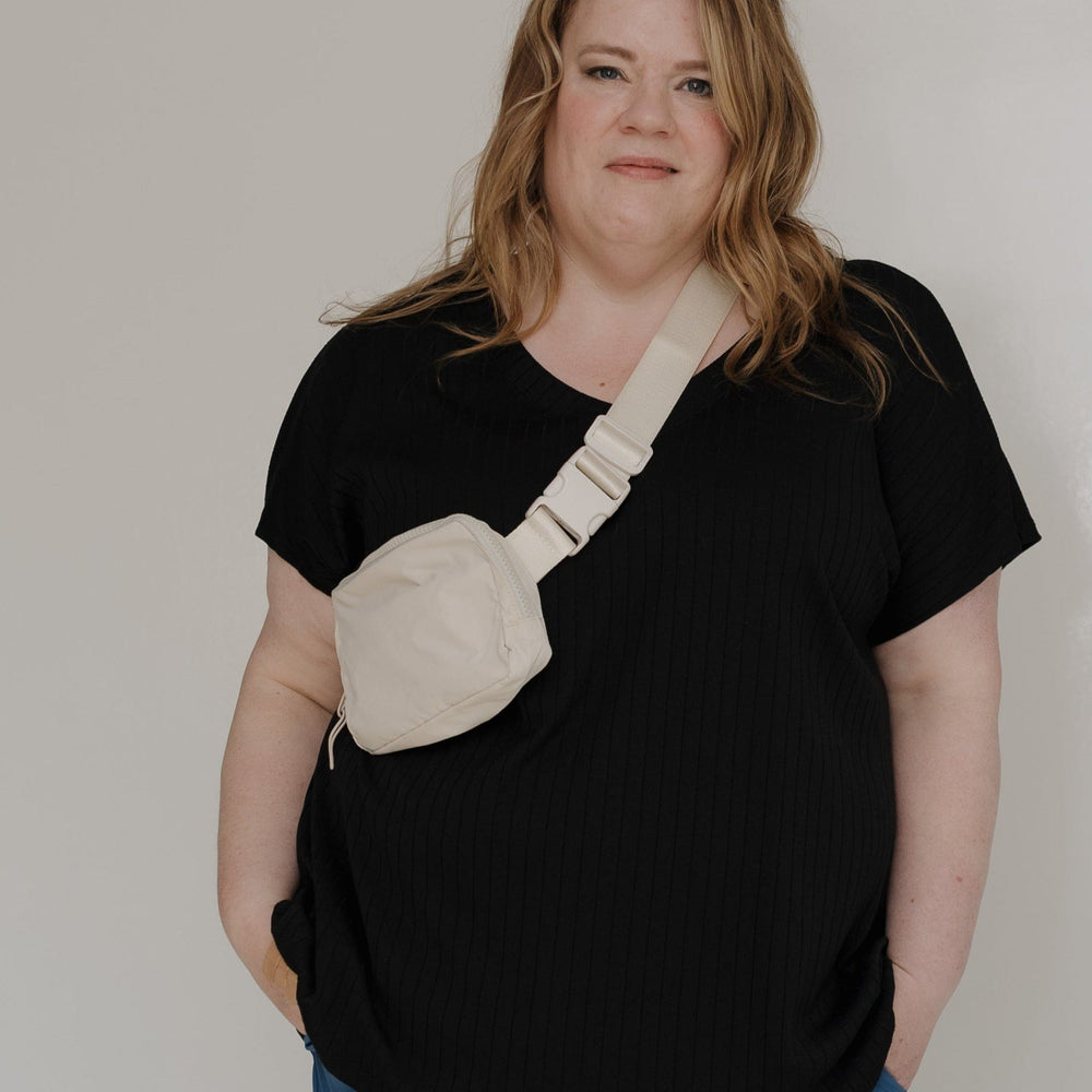 Person wearing a black t-shirt with a beige bag design and blue pants against a white background