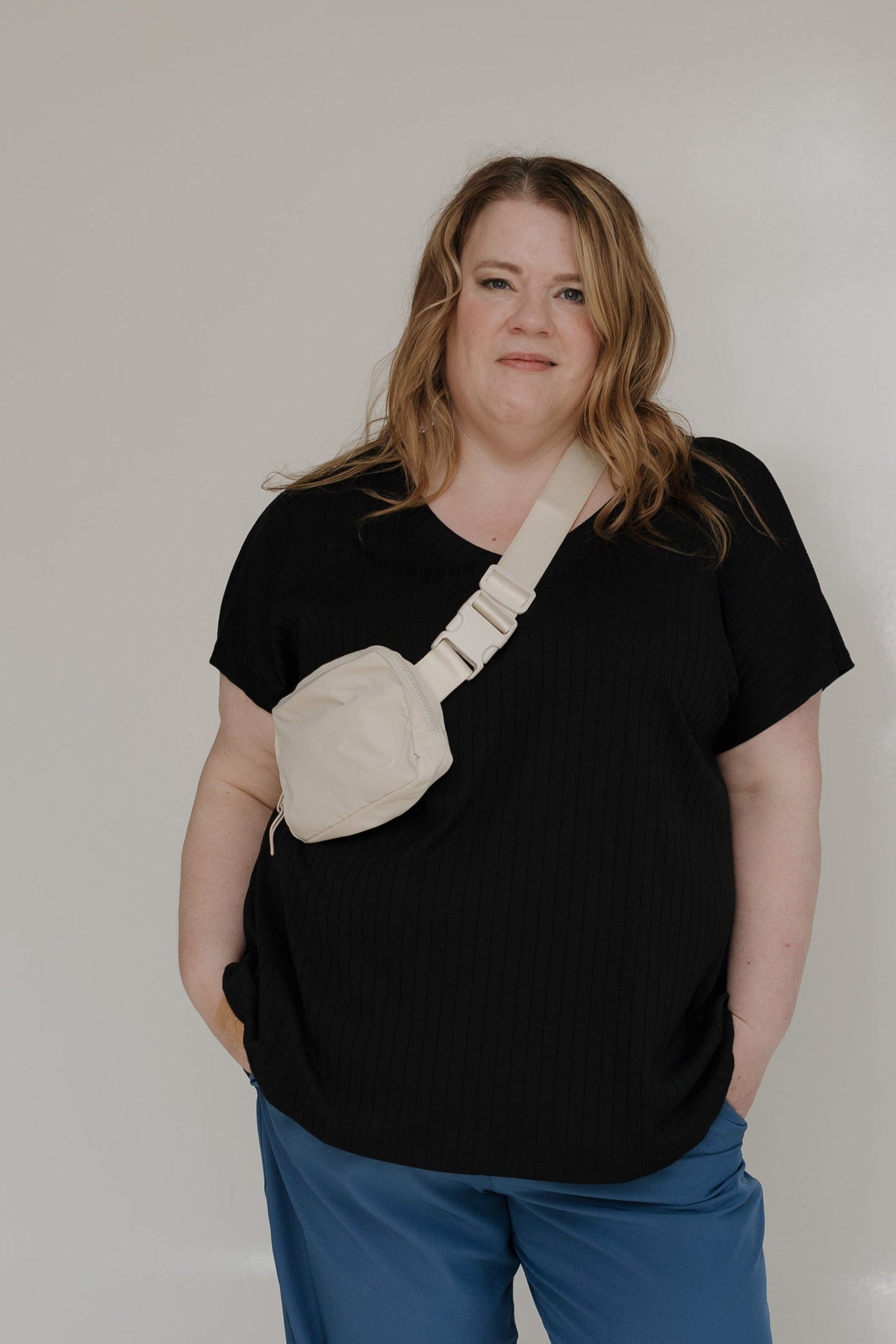 Person wearing a black t-shirt with a beige bag design and blue pants against a white background