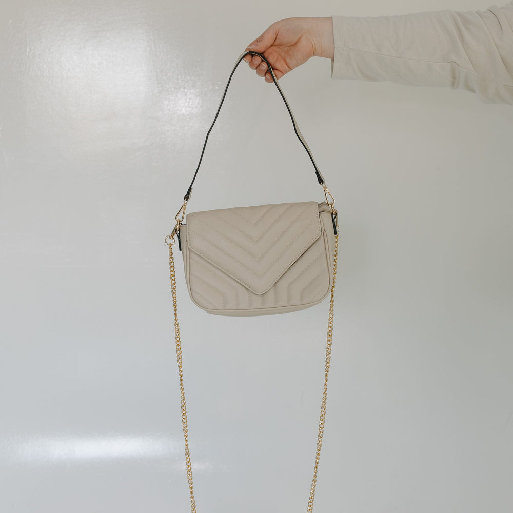 Beige quilted handbag with a chain strap held by a person against a light background