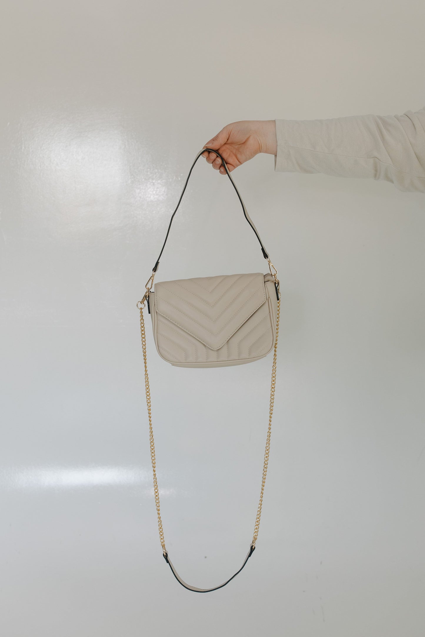 Beige quilted handbag with a chain strap held by a person against a light background