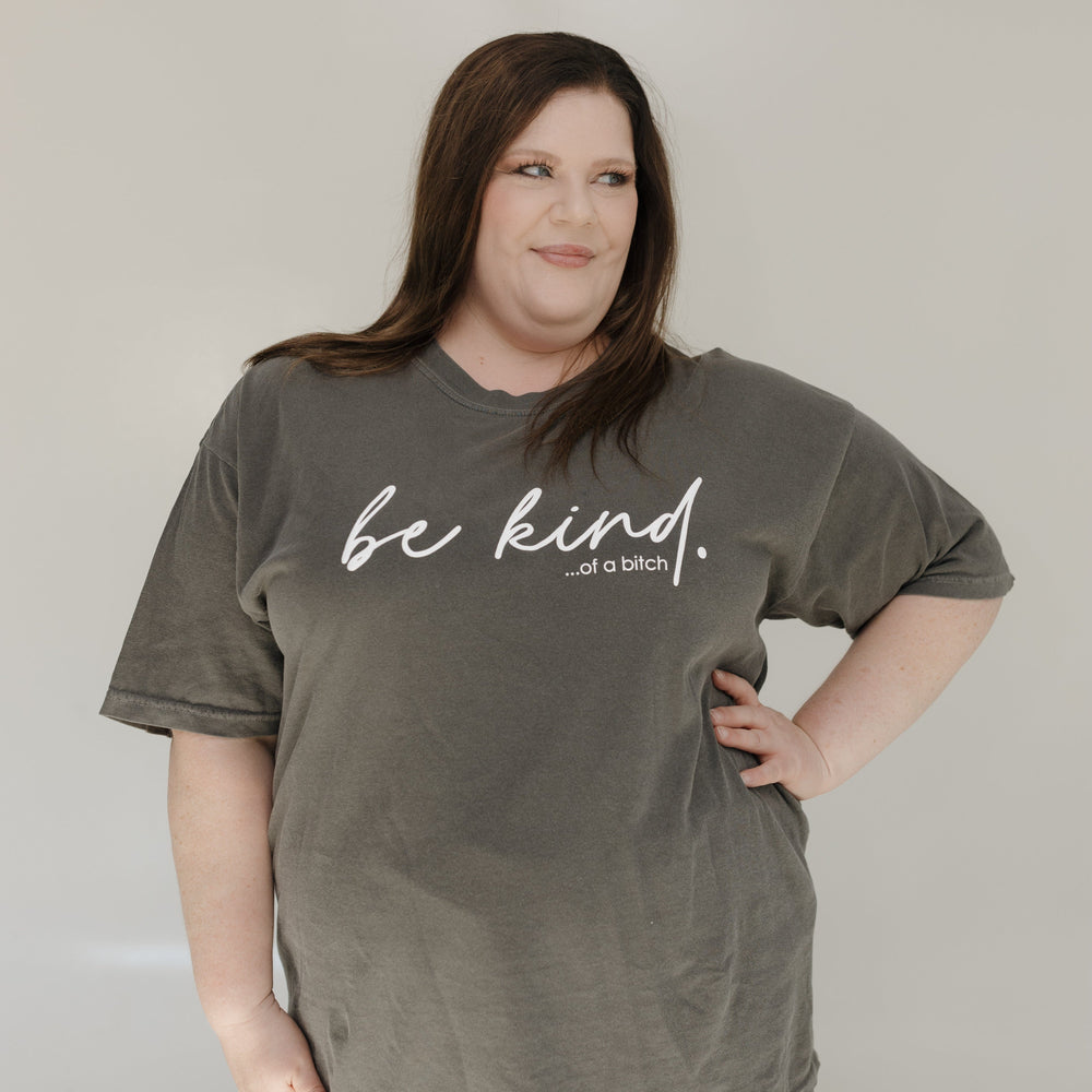 Person wearing a green t-shirt with 'be kind... of a bitch' text against a plain background