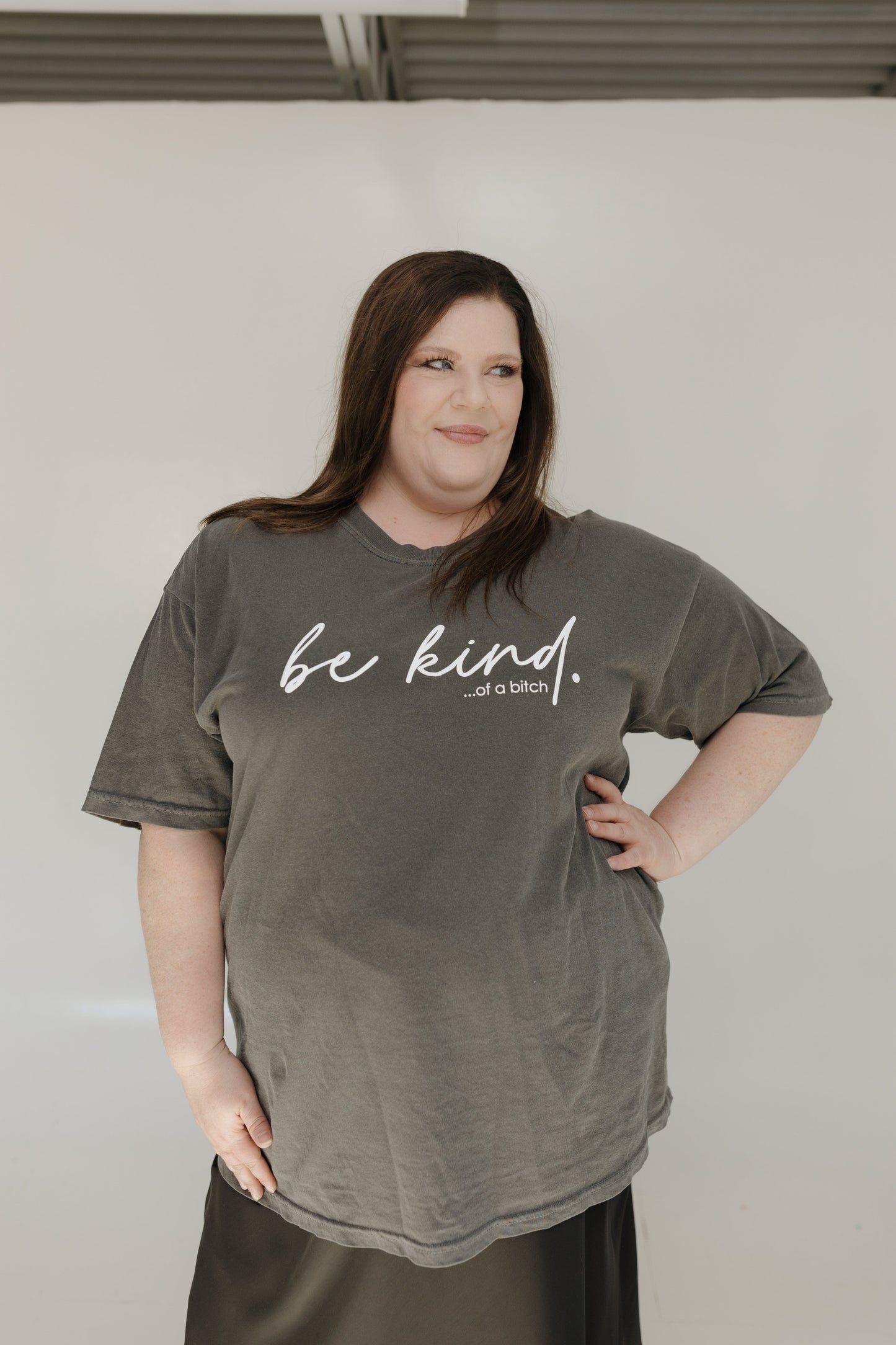 Person wearing a green t-shirt with 'be kind... of a bitch' text against a plain background