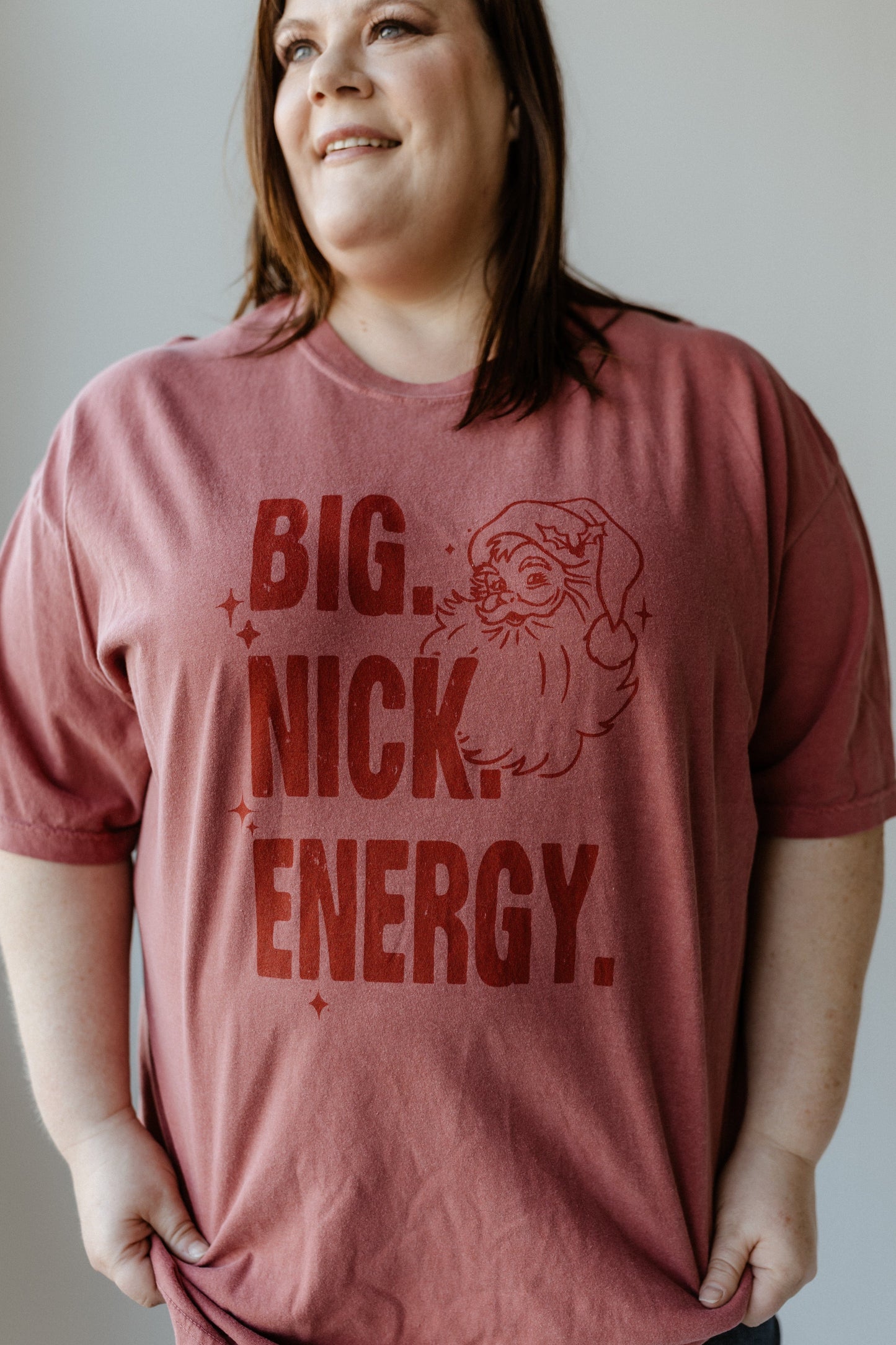 A person wearing a garment-dyed shirt featuring a Santa graphic with the bold text "BIG. NICK. ENERGY." This festive graphic tee adds a playful twist to holiday fashion, perfect for making a jolly statement.