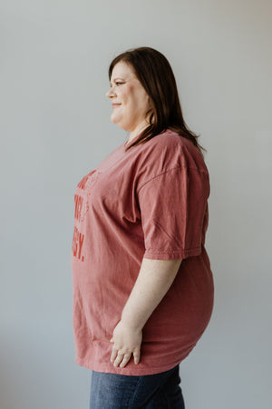 A woman in a graphic tee and jeans stands sideways against a plain background.