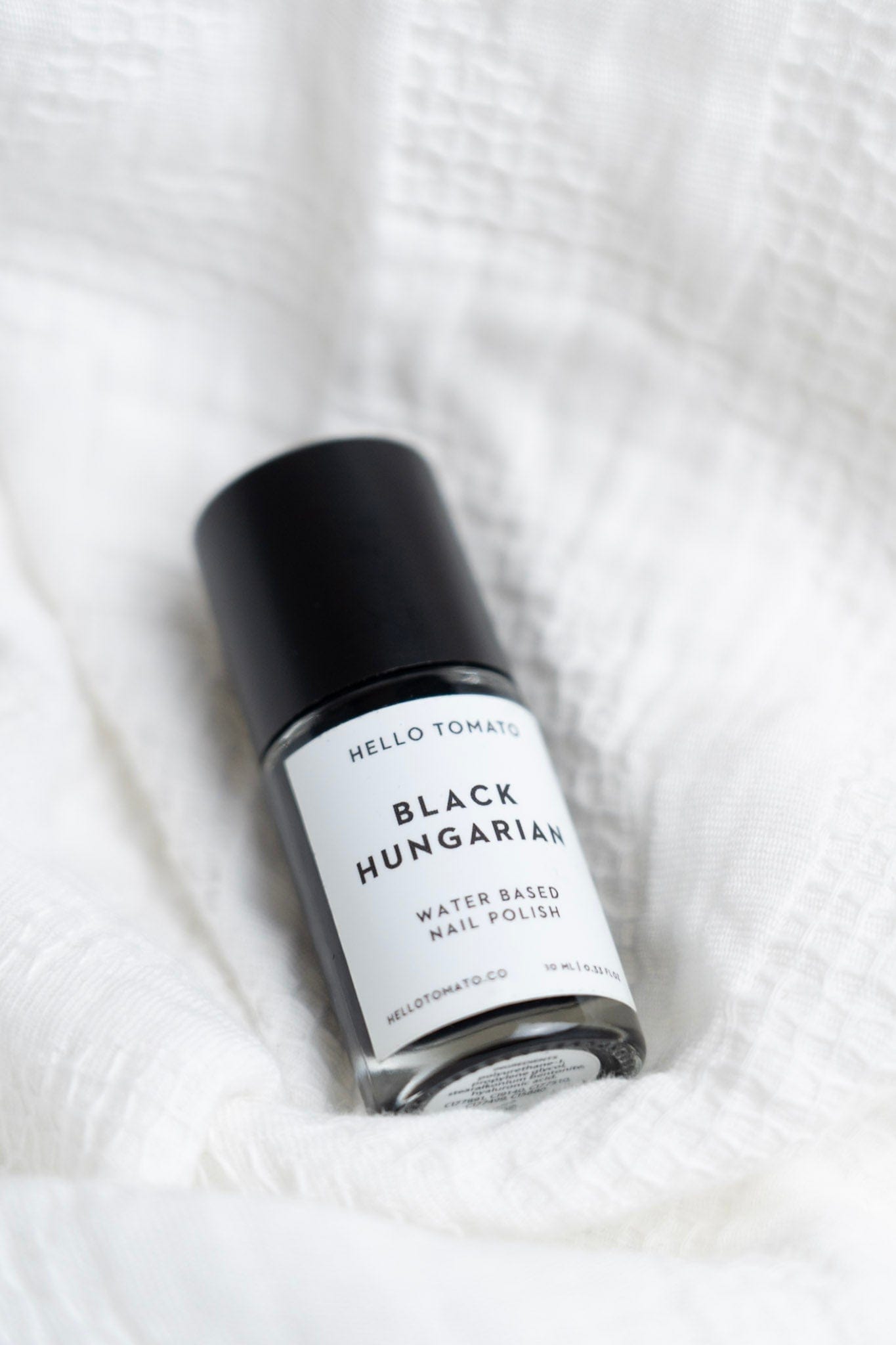 Black Hungarian water-based nail polish bottle on a white textured background