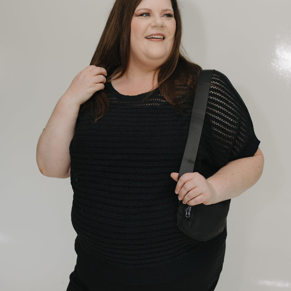 Woman wearing a black outfit with a shoulder bag against a plain background