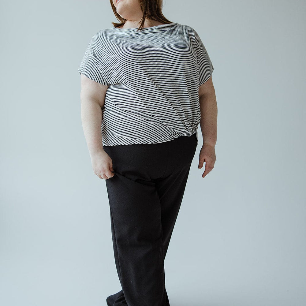 A person stands wearing a striped shirt and sleek dress pants made from lightweight fabric, looking to the side against a plain background.