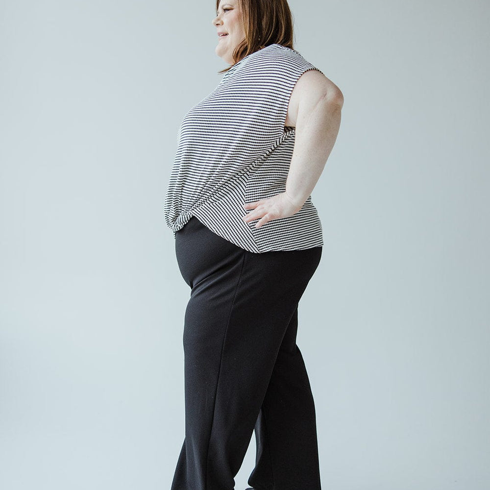 A woman in a striped sleeveless top and sleek dress pants, made from lightweight fabric, stands in a side pose against a plain background.