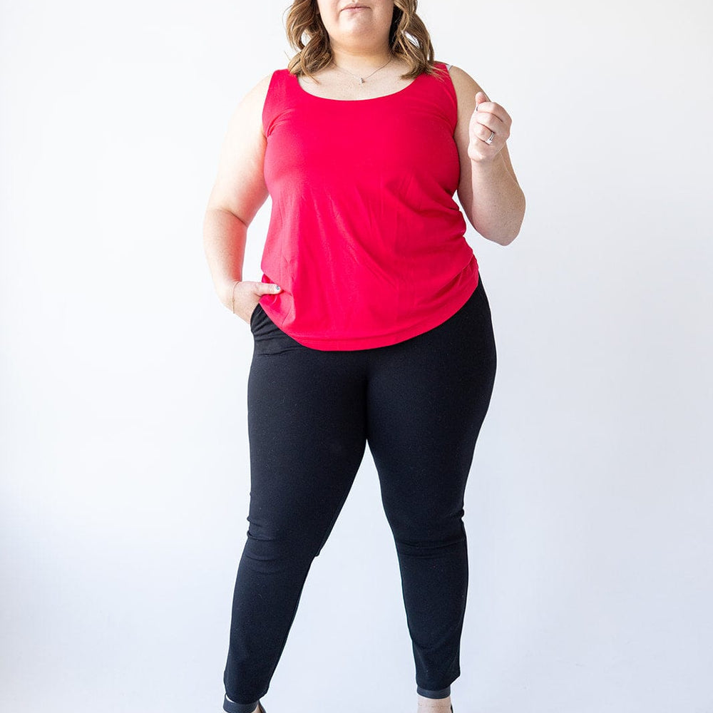 A woman in a red sleeveless top and elegant black dress pants, made from a luxury fabric, stands against a white background.