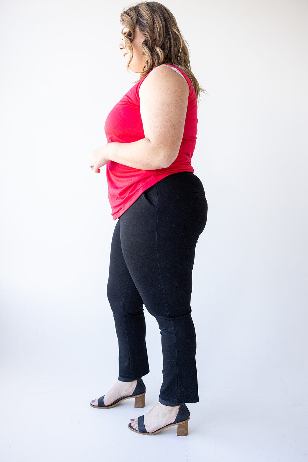 A person in a red sleeveless top and black dress pants stands sideways against a white background, showcasing the luxury fabric and wearing black sandals.