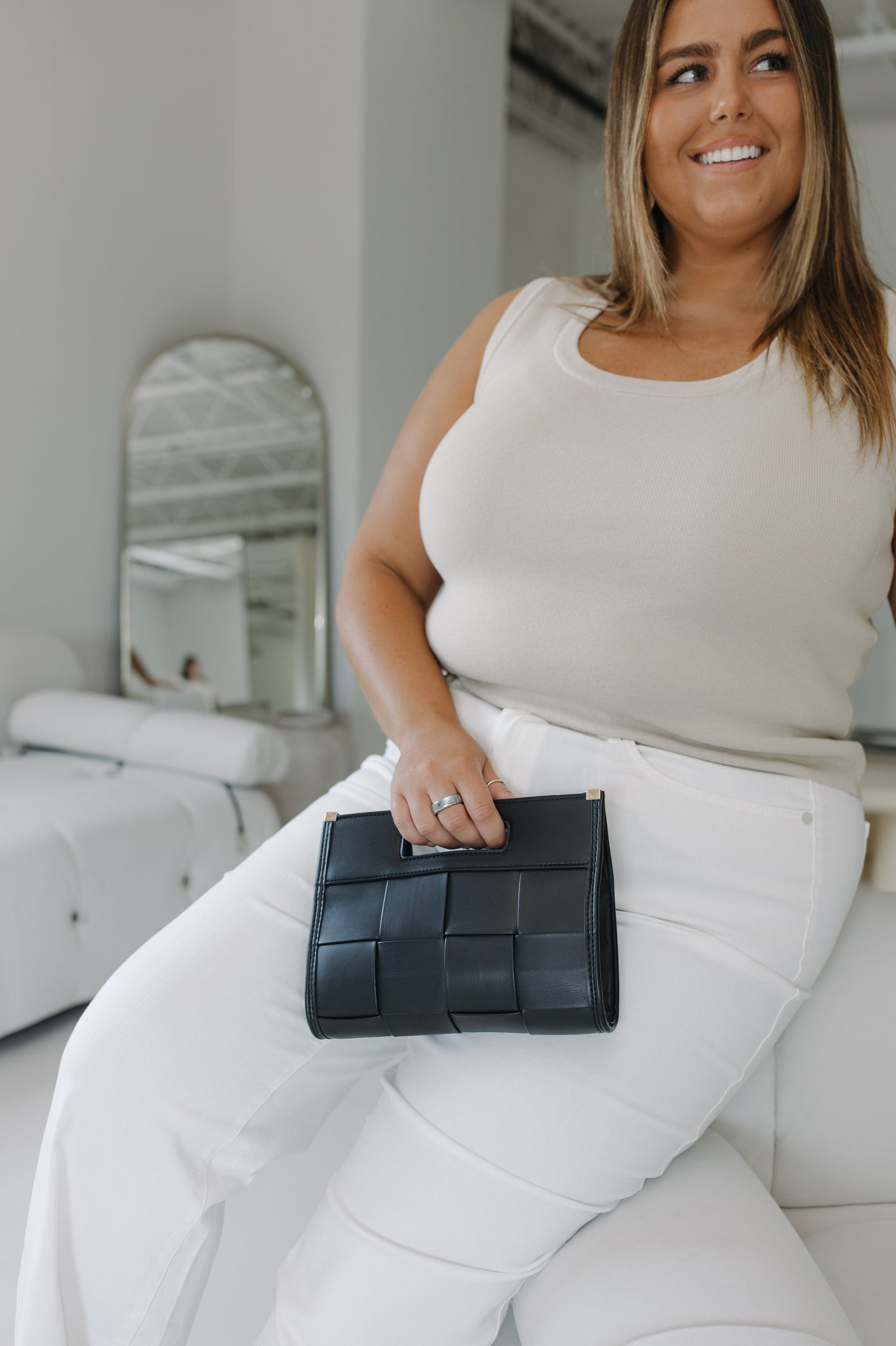 Woman holding a black woven clutch in a minimalistic room.