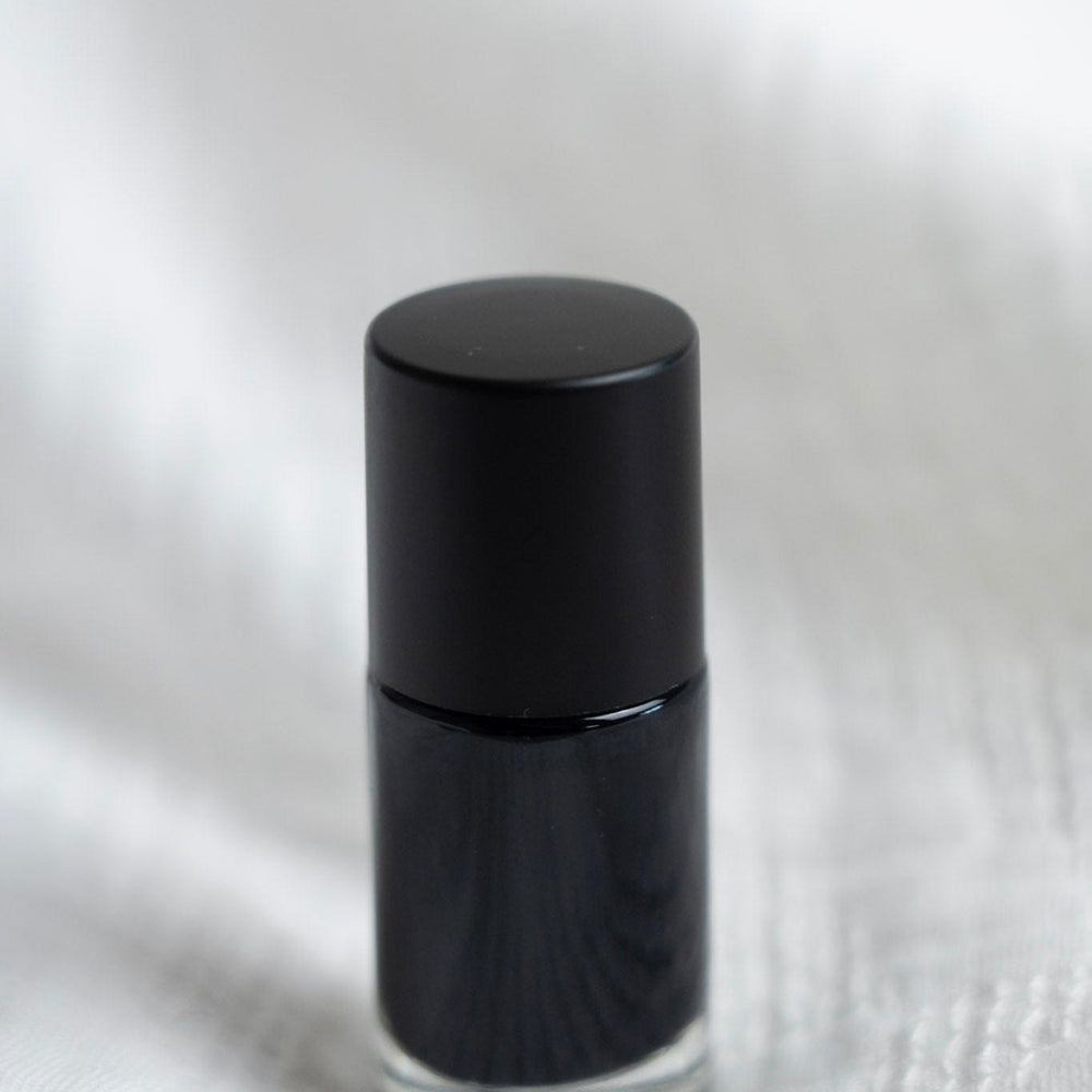 Black nail polish bottle on a white textured surface