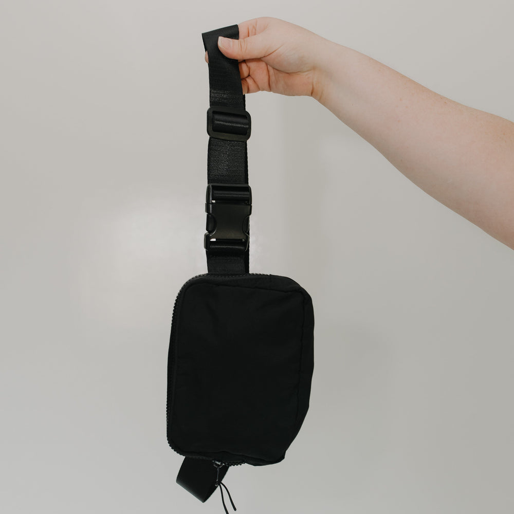 Black waist bag held by a hand against a plain background