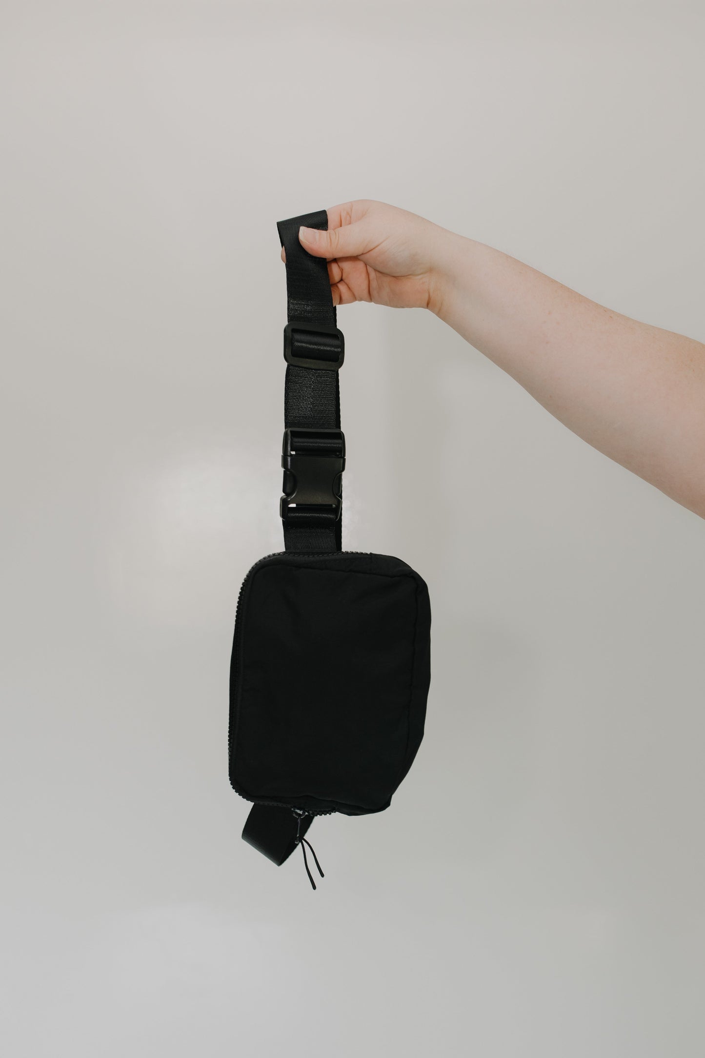 Black waist bag held by a hand against a plain background