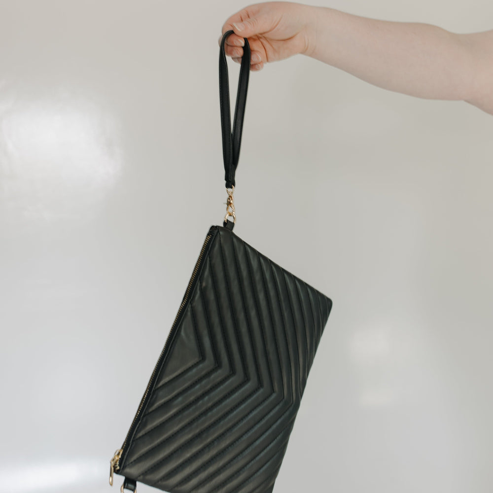 Black textured clutch bag held by a hand against a light background