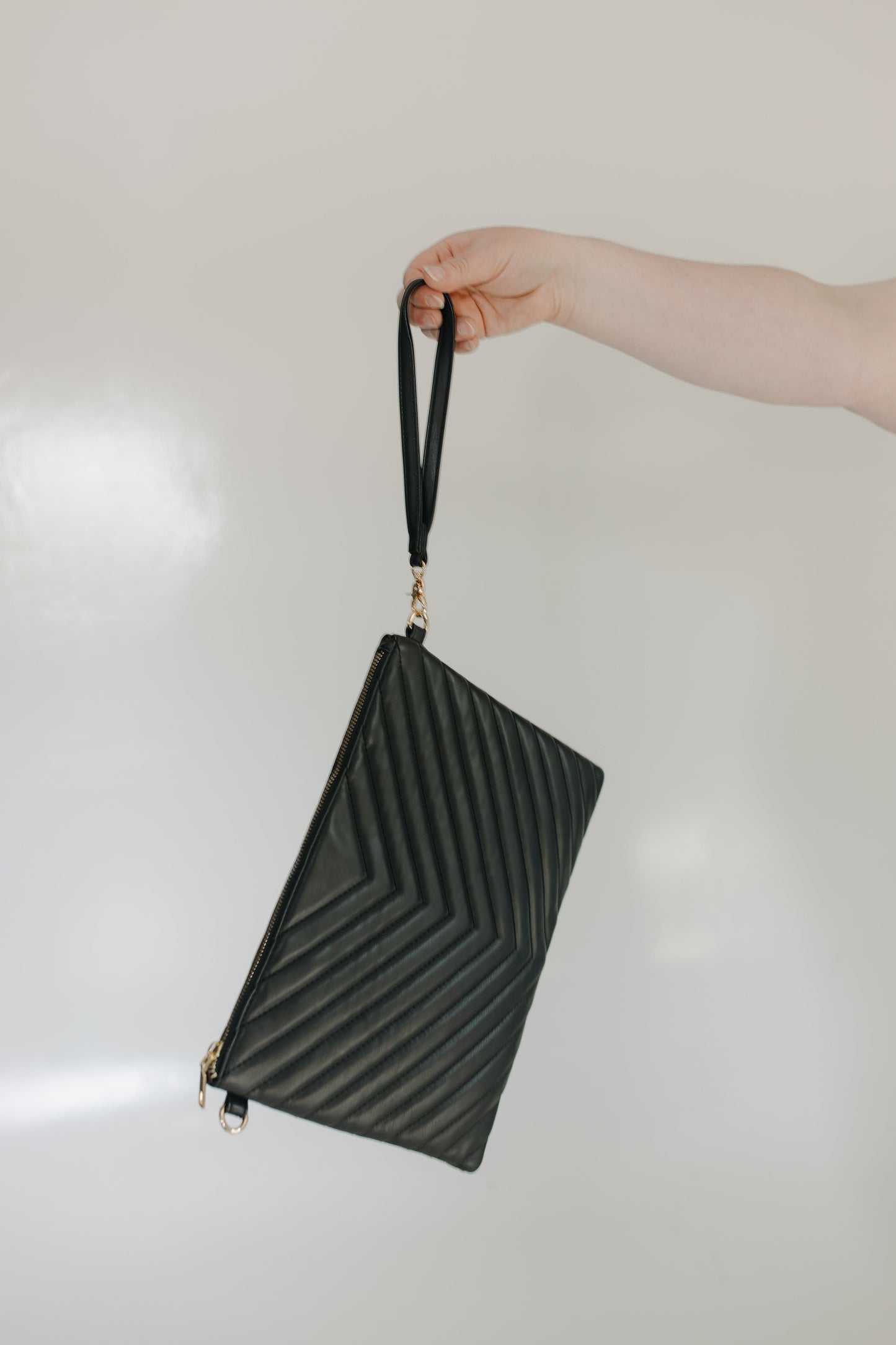 Black textured clutch bag held by a hand against a light background