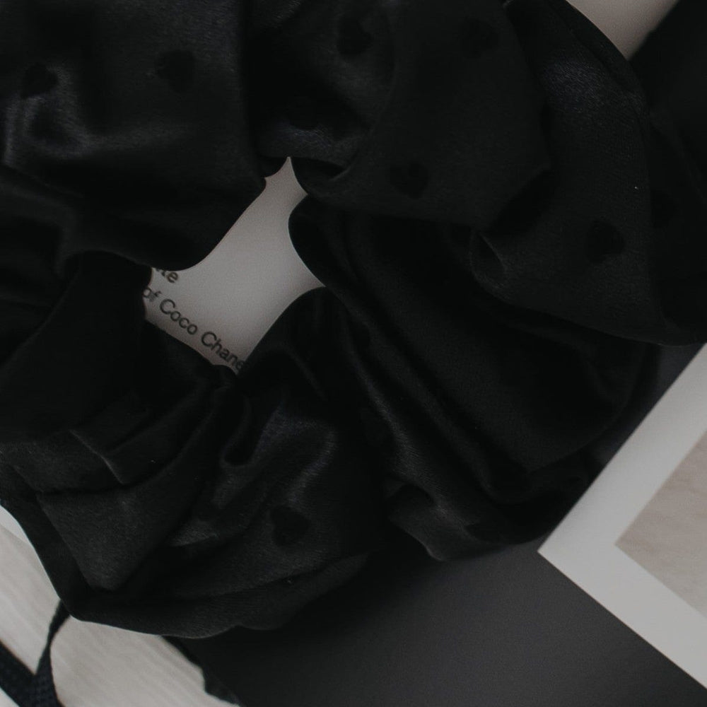 Black scrunchie on a white surface with text in the background