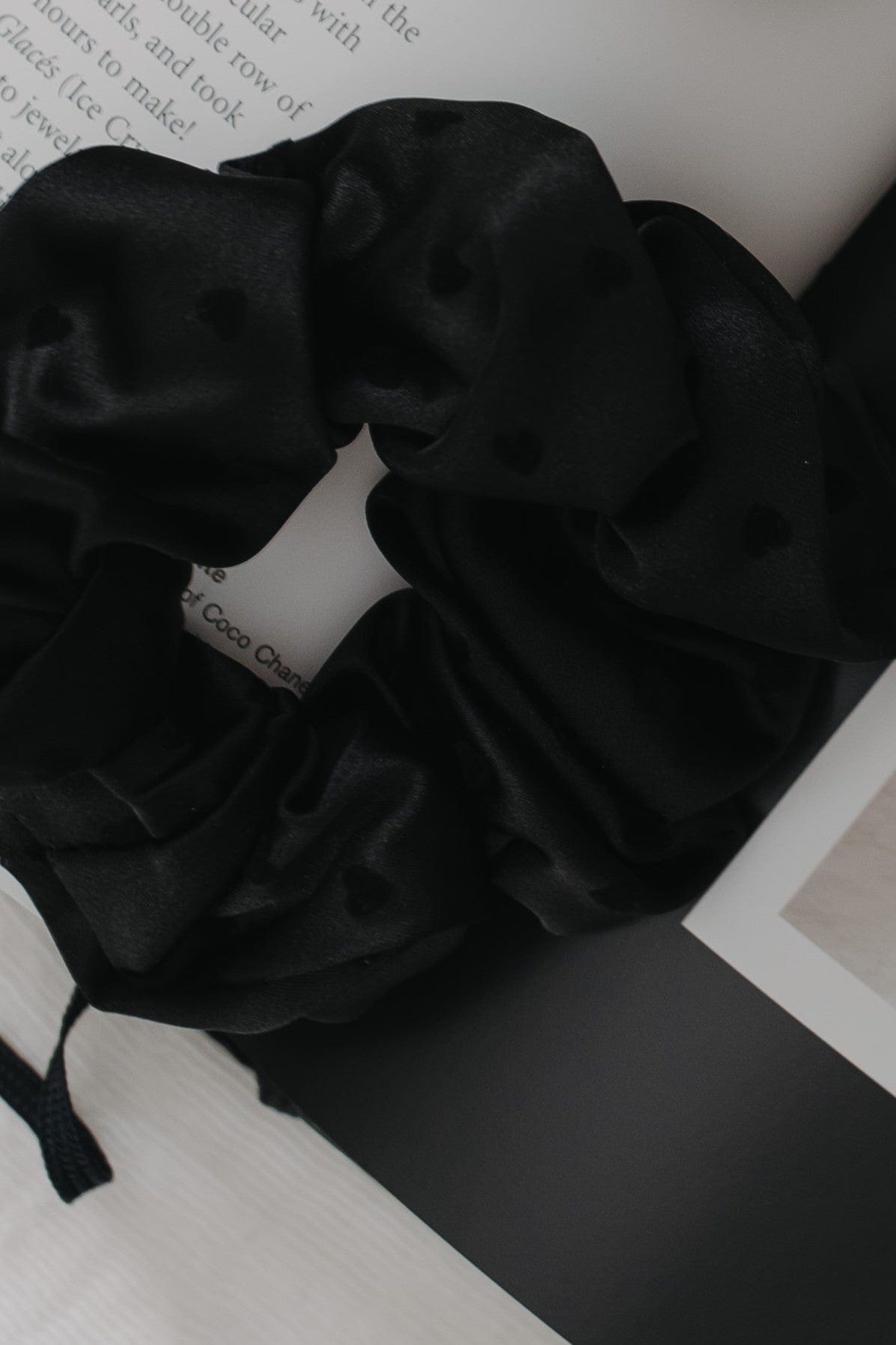 Black scrunchie on a white surface with text in the background