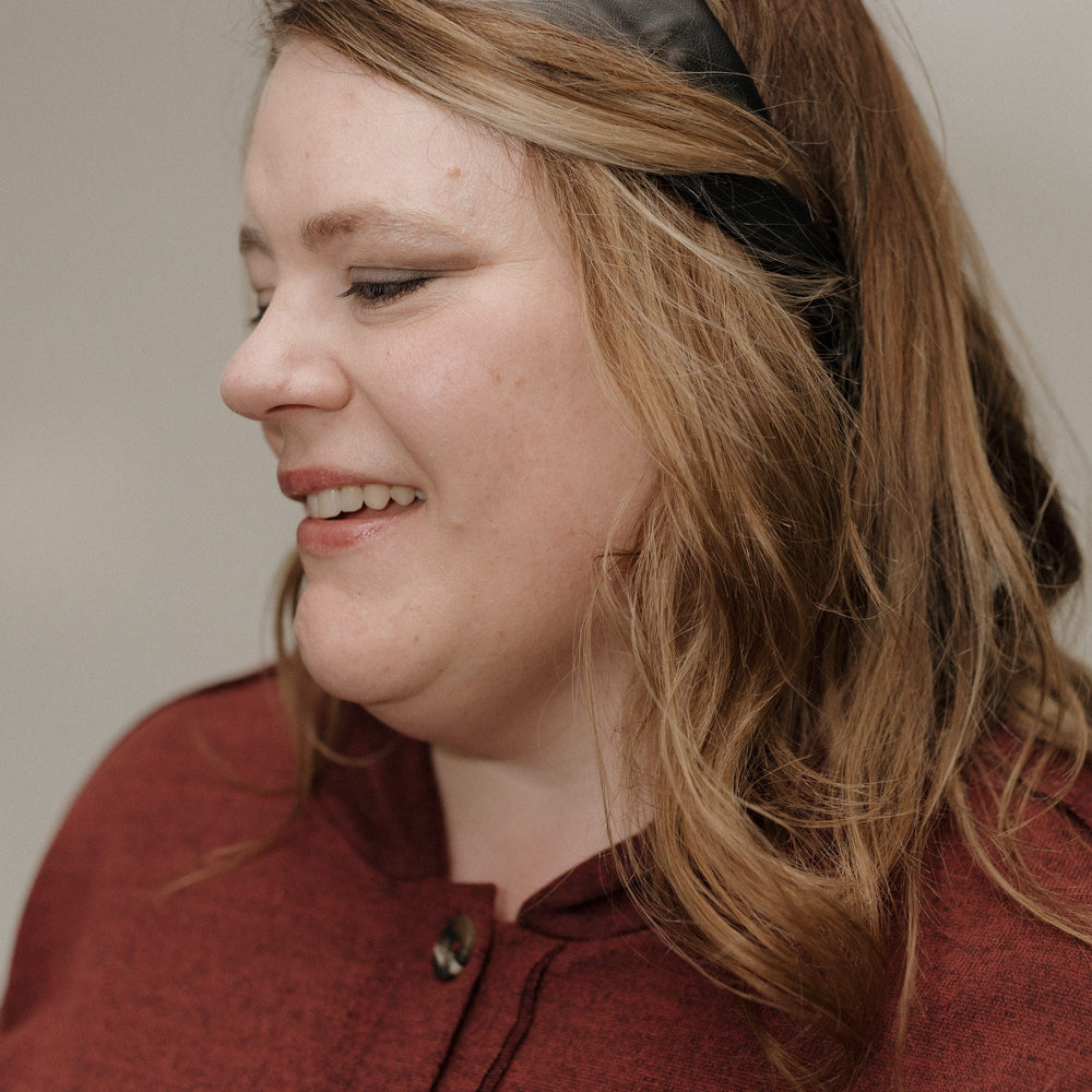 Woman wearing a red coat and black headband against a neutral background