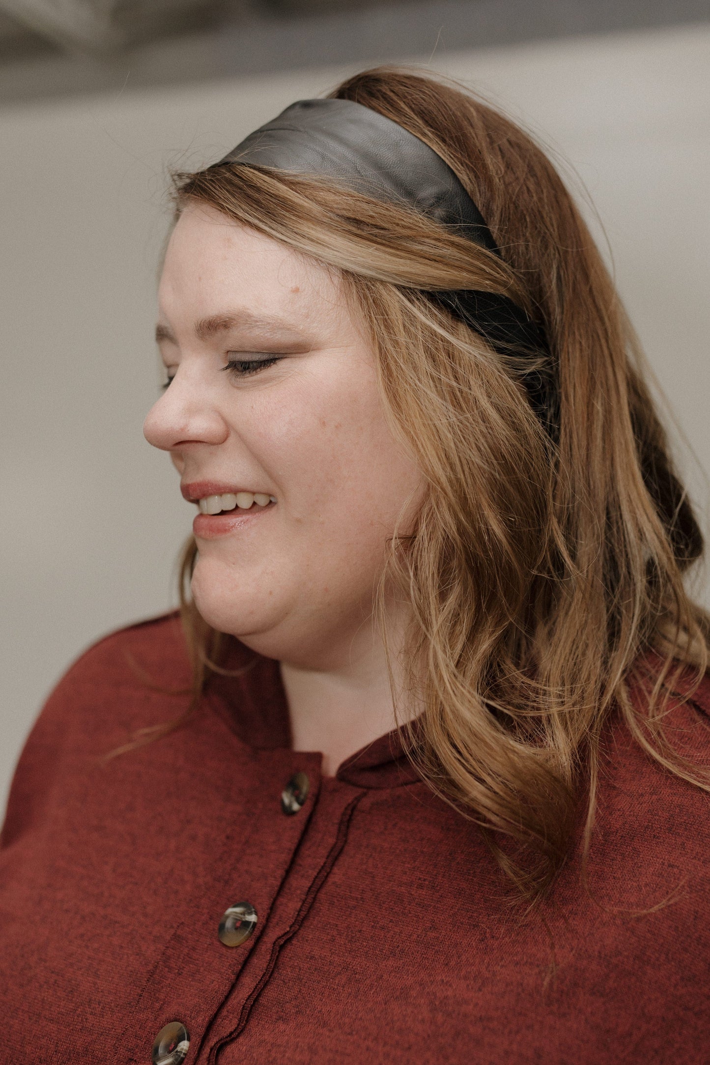 Woman wearing a red coat and black headband against a neutral background