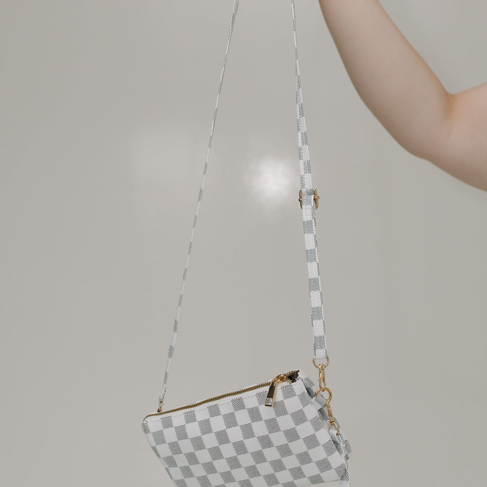 Black and white checkered handbag with a strap held by a hand against a plain background