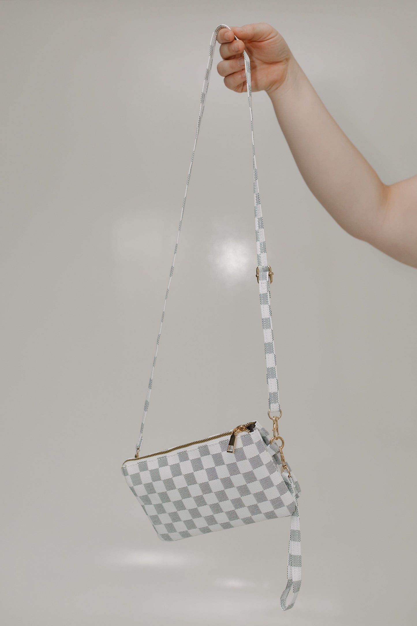 Black and white checkered handbag with a strap held by a hand against a plain background