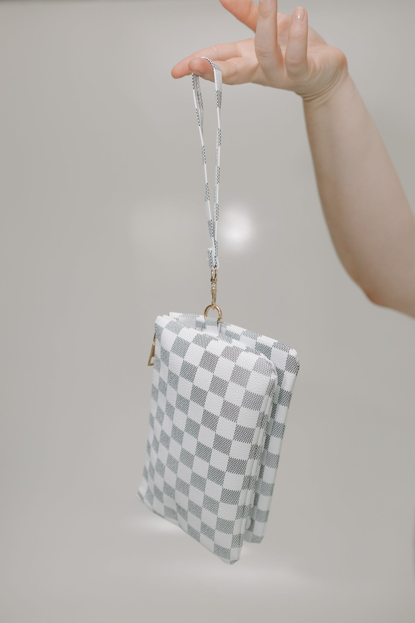 Checkered handbag with a strap held by a hand against a neutral background