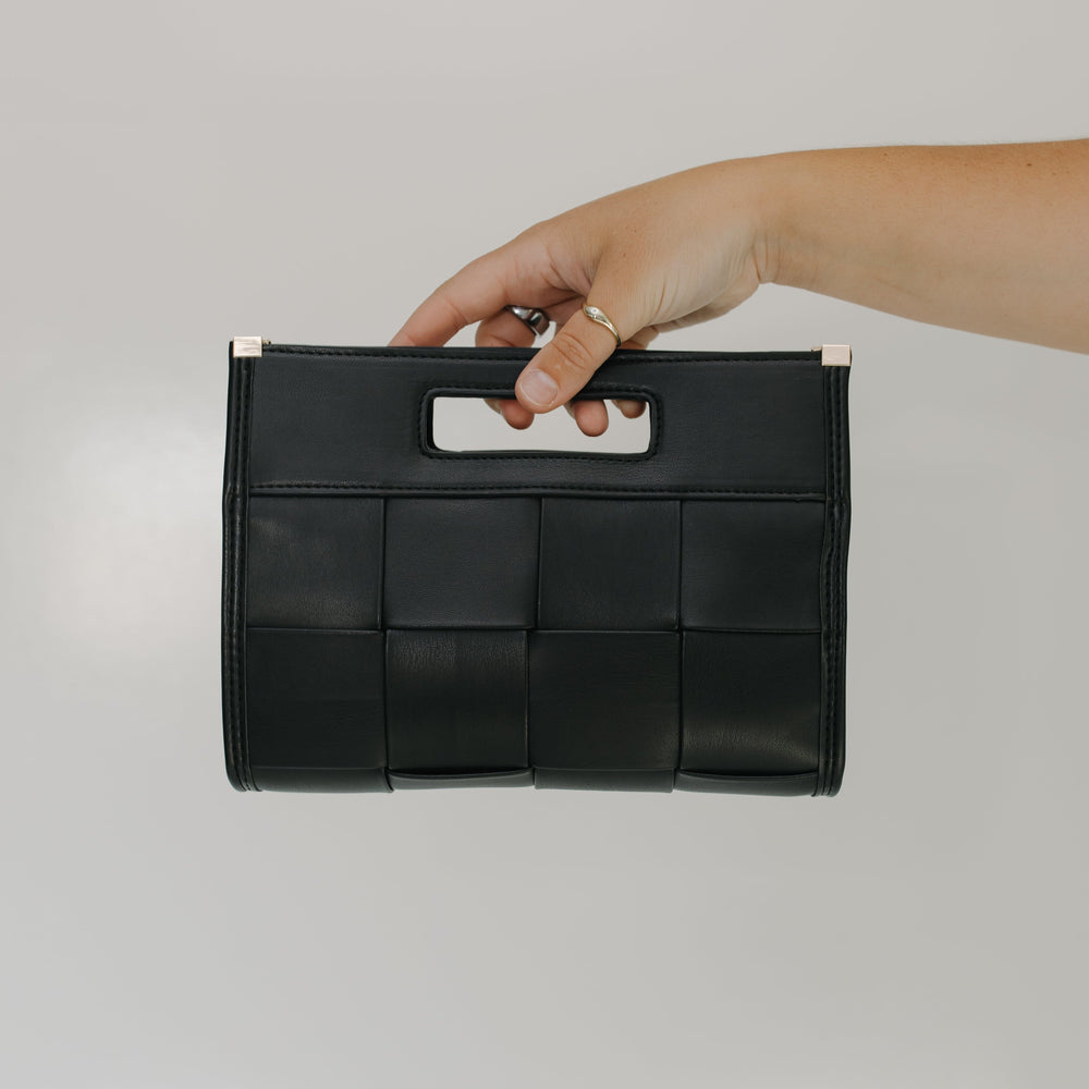 Black woven handbag held by a hand against a gray background