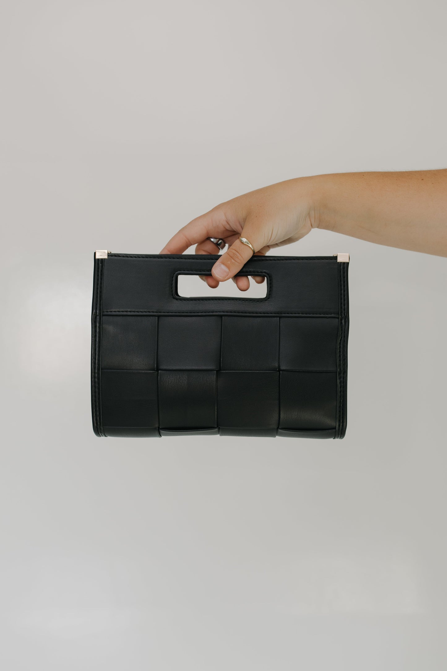 Black woven handbag held by a hand against a gray background