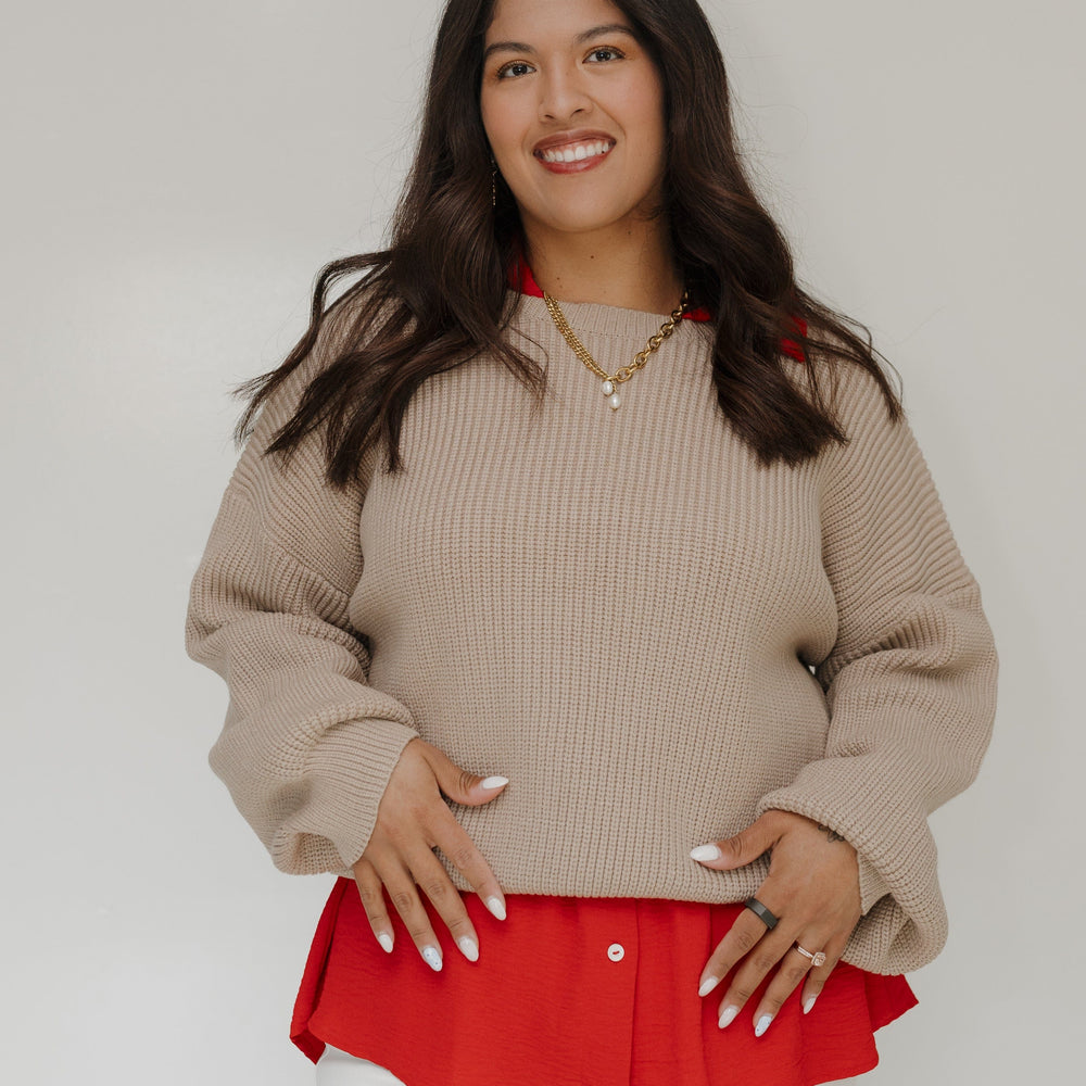 Woman wearing a beige sweater over a red top with a plain background