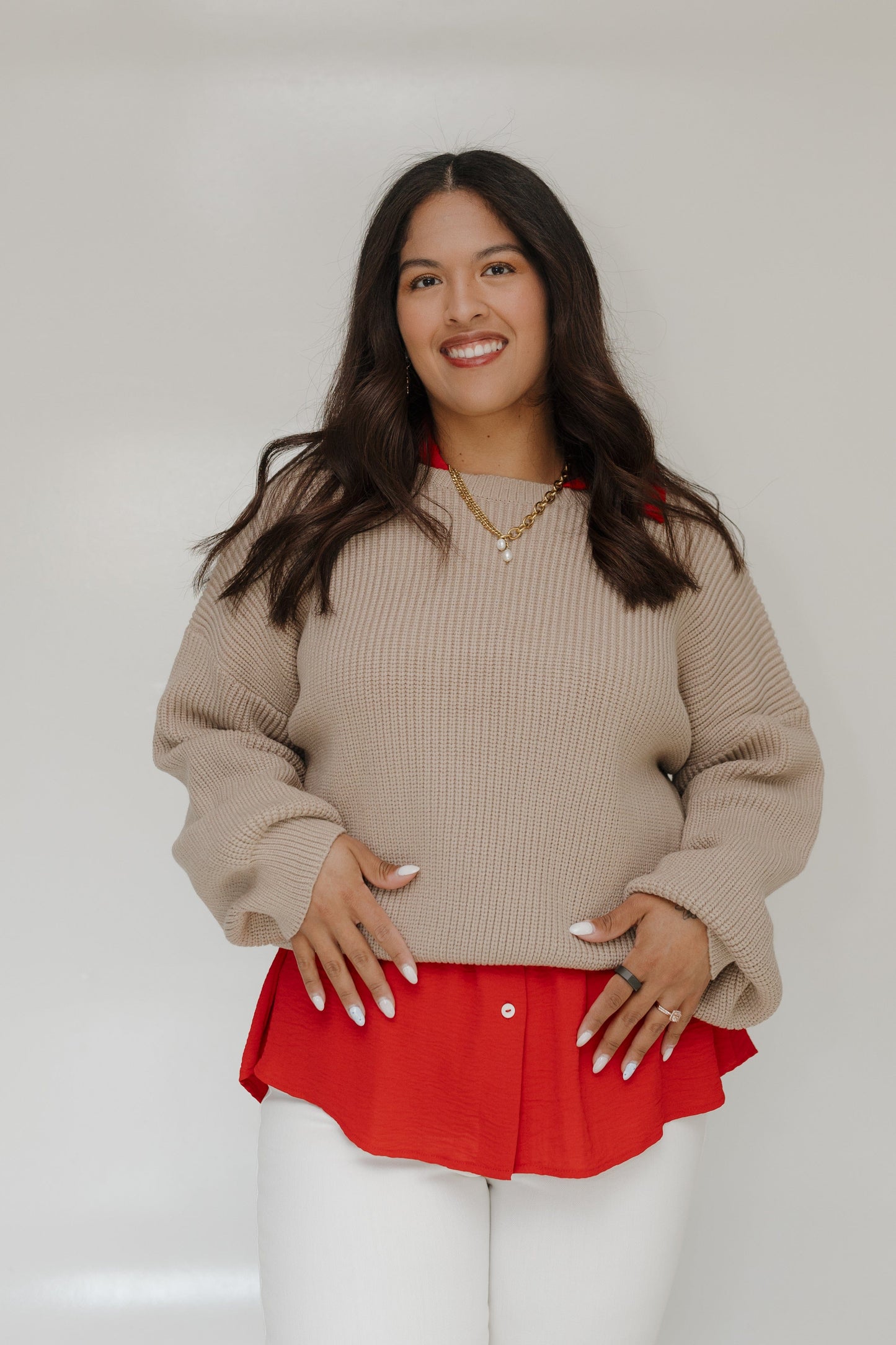 Woman wearing a beige sweater over a red top with a plain background