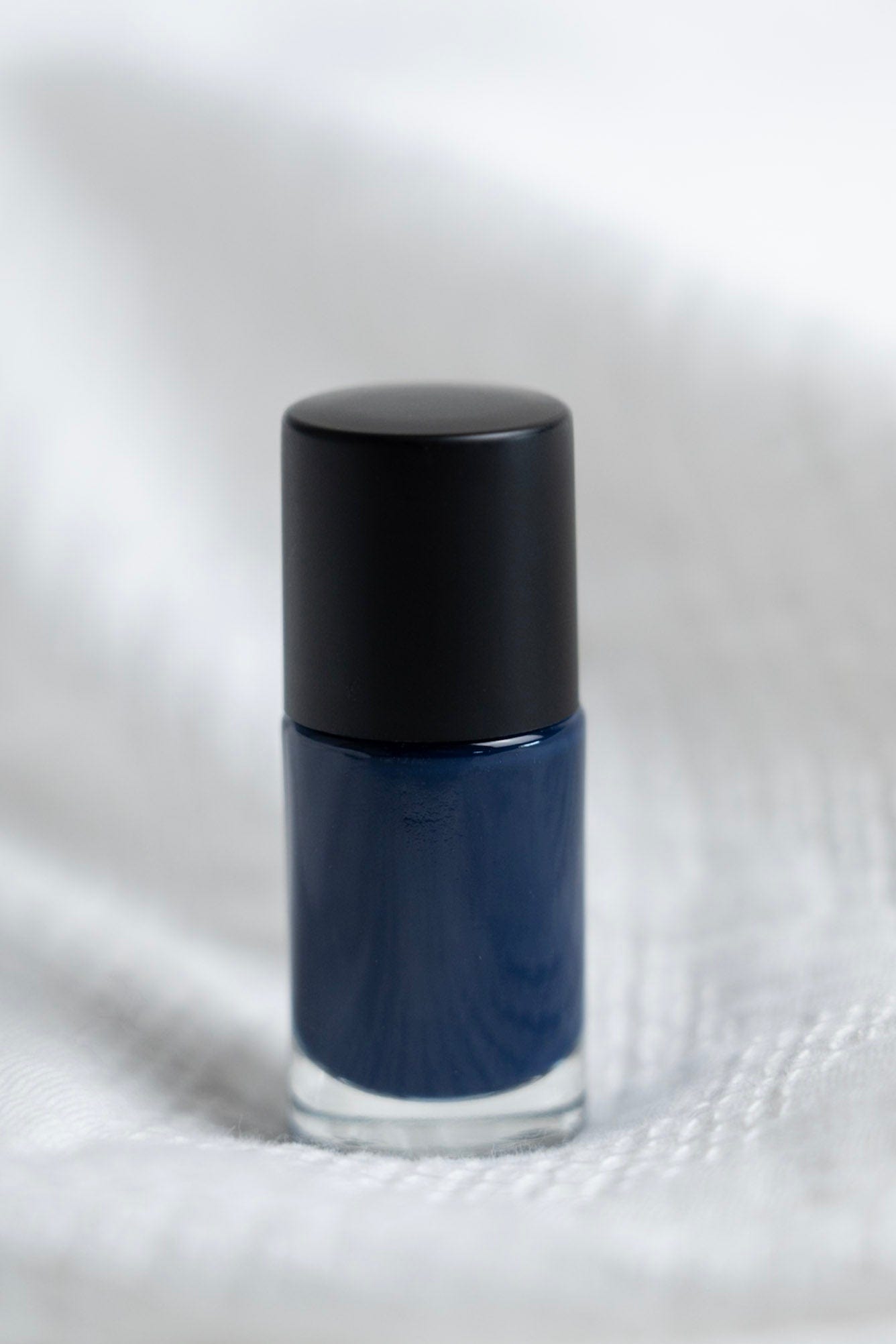 Blue nail polish bottle with black cap on a white fabric background