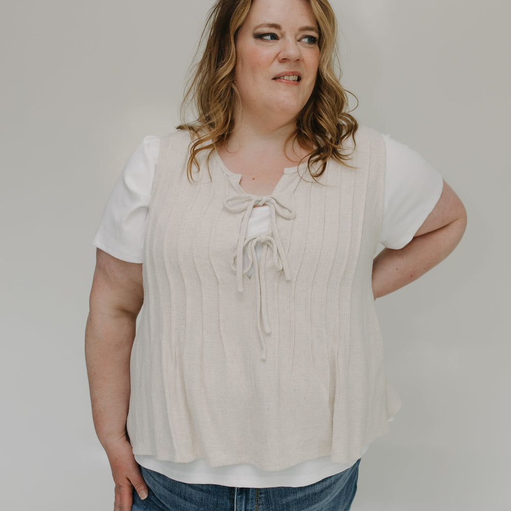 Woman wearing a beige blouse and blue jeans against a plain background