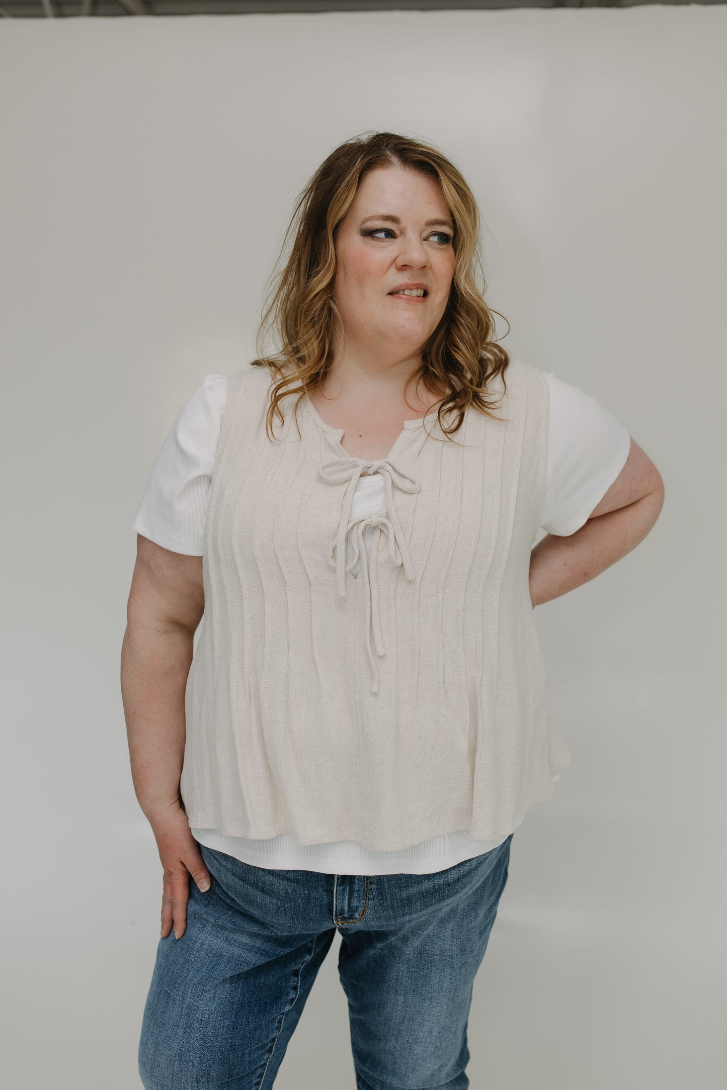 Woman wearing a beige blouse and blue jeans against a plain background