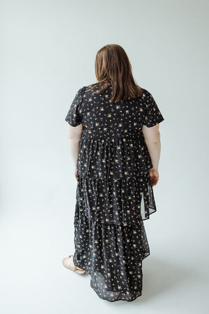 Turning away against a simple light background, a person models the BOHO LAYERED RUFFLE DRESS by Mikarose, an elegant black floral piece exuding Bohemian flair.