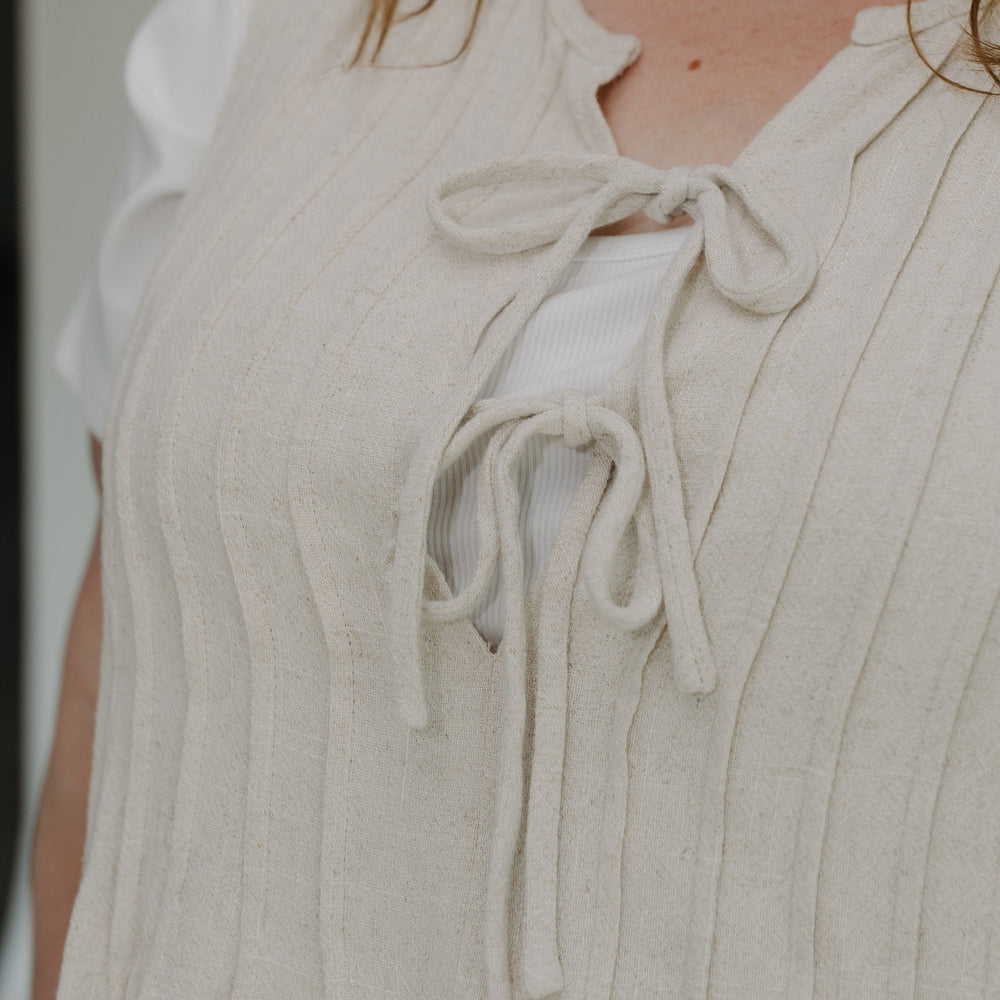 Close-up of a person wearing a light-colored sleeveless top with lace-up front.