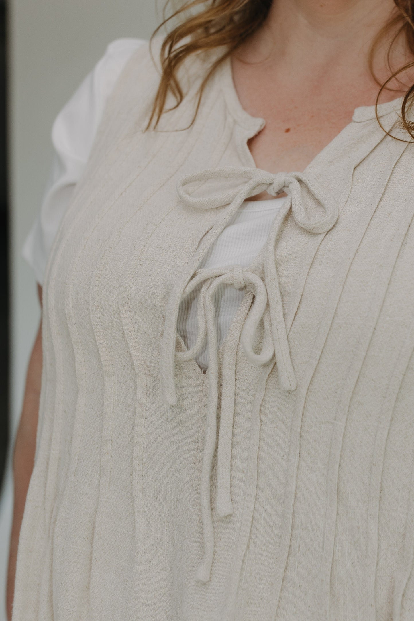 Close-up of a person wearing a light-colored sleeveless top with lace-up front.