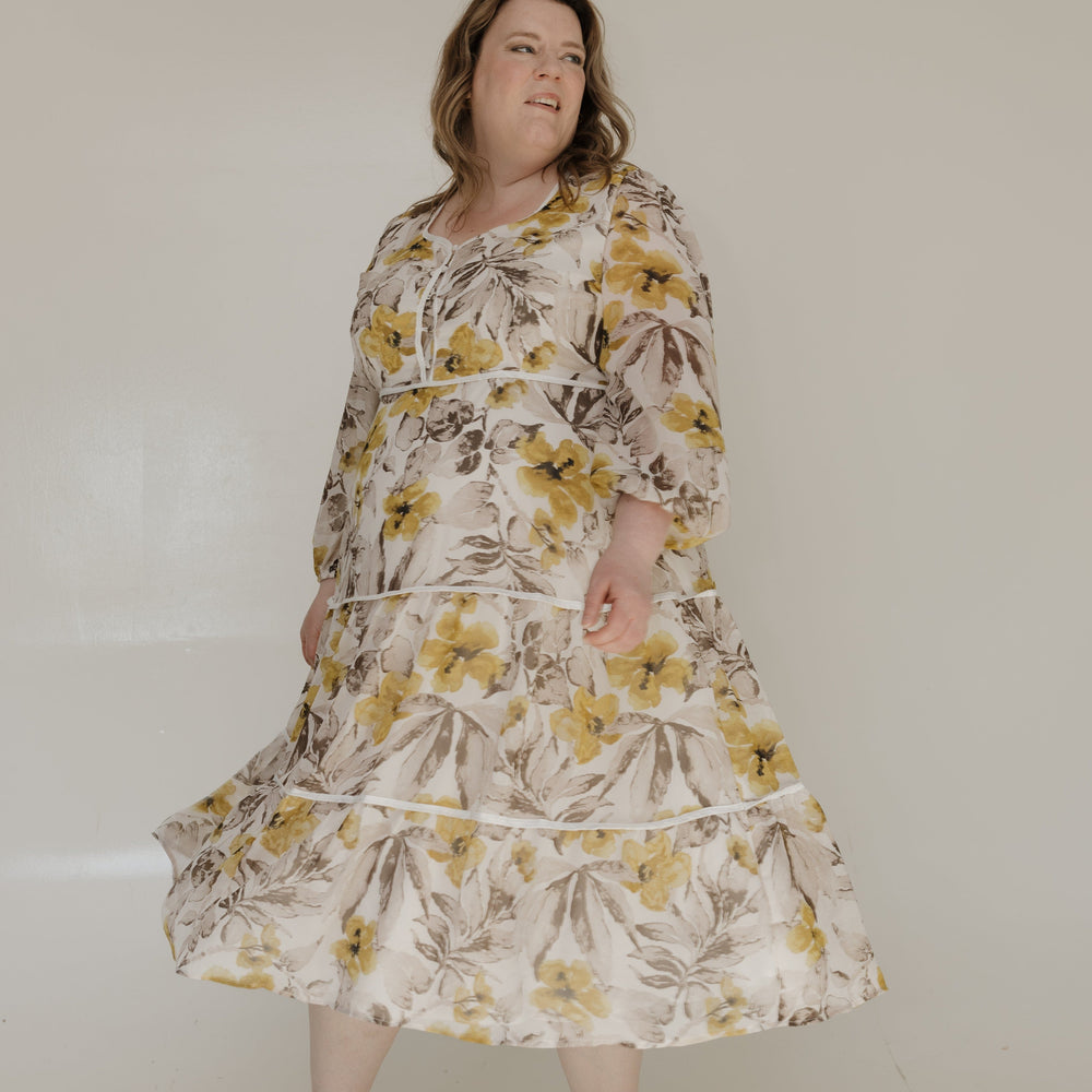 Woman wearing a floral dress standing against a plain background