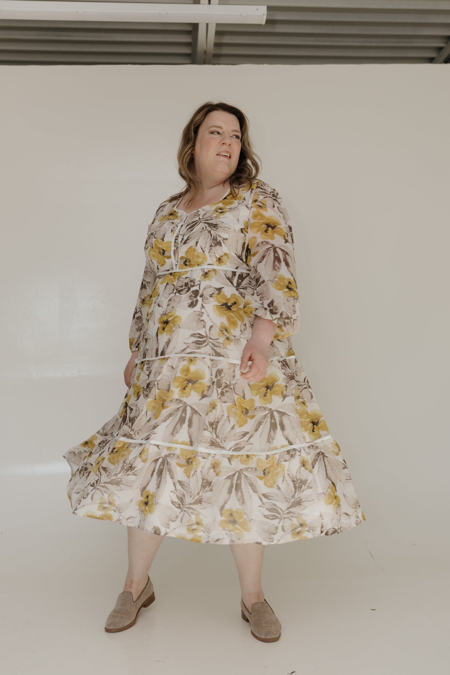 Woman wearing a floral dress standing against a plain background