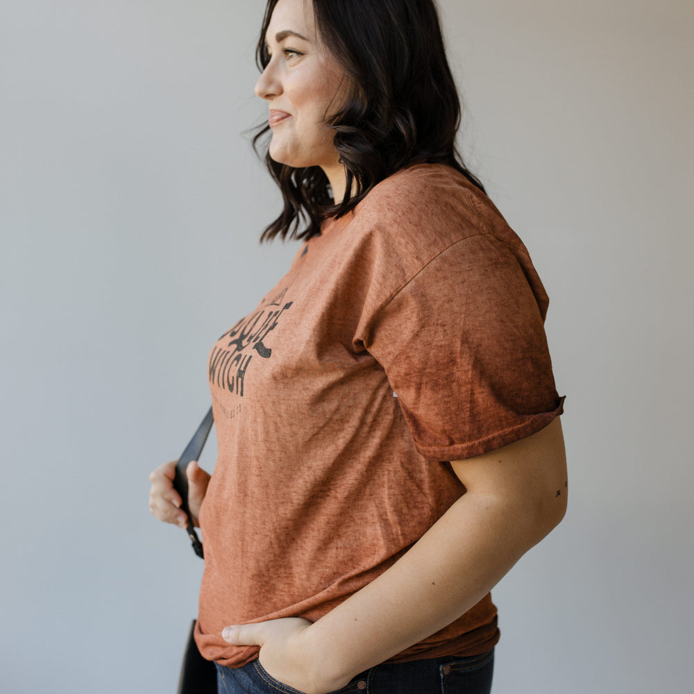 A person in profile, wearing the "BOUJEE WITCH" GRAPHIC TEE by Love Marlow paired with jeans, stands with one hand in a pocket against a plain background.