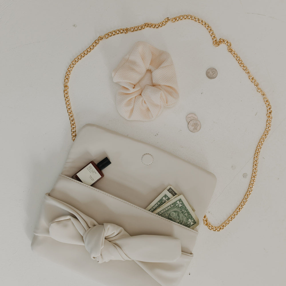 White handbag with gold chain, money, and a bow on a light gray background