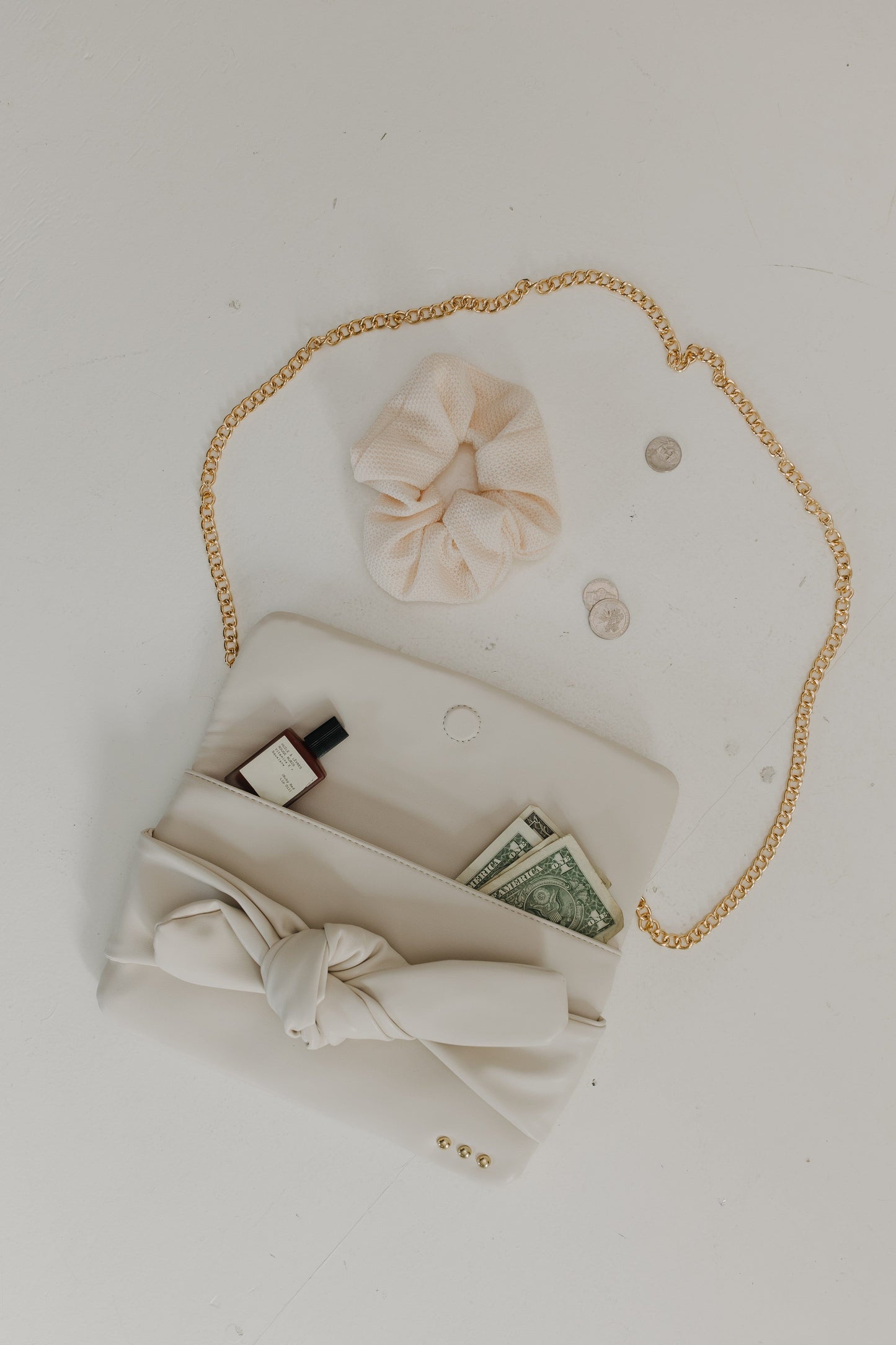 White handbag with gold chain, money, and a bow on a light gray background
