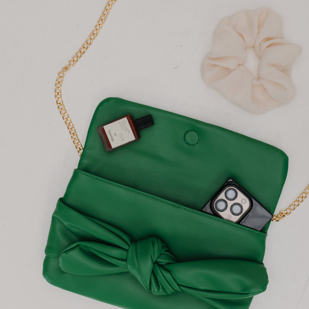 Green clutch bag with a knot detail on a light gray background