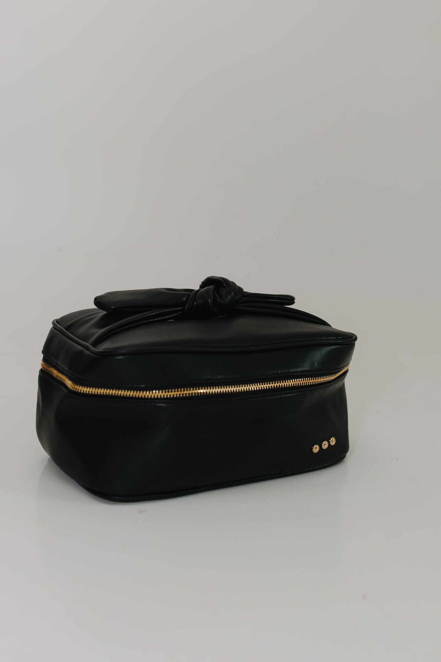 Black cosmetic bag with gold zipper on a light gray background