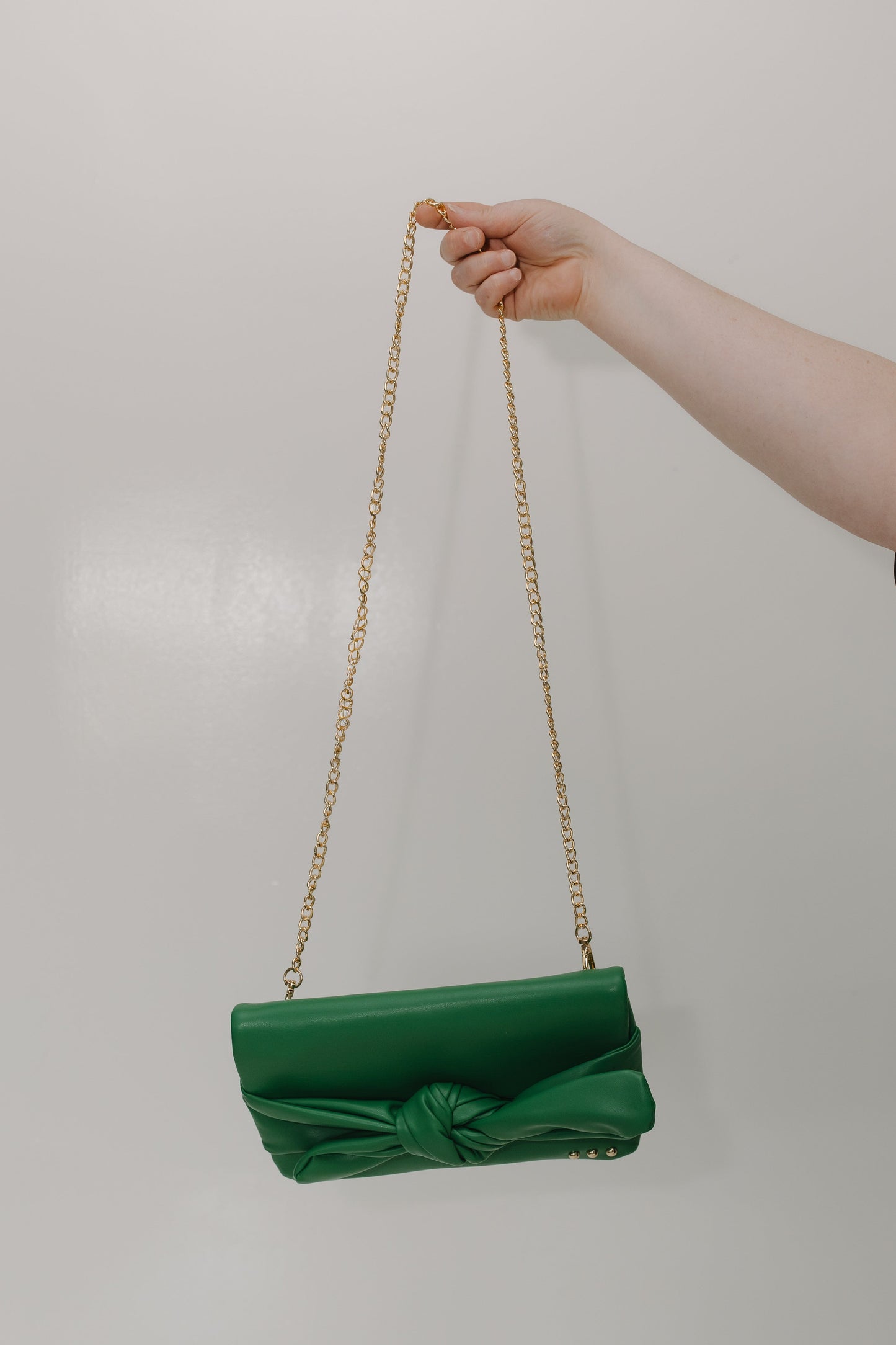 Green handbag with a gold chain strap held by a hand against a plain background