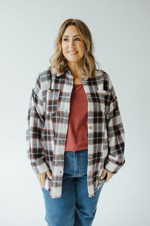 A woman stands against a plain background, wearing the Love Marlow's Boyfriend Shacket with Frayed Hem in Black Checkered over a red top and jeans.