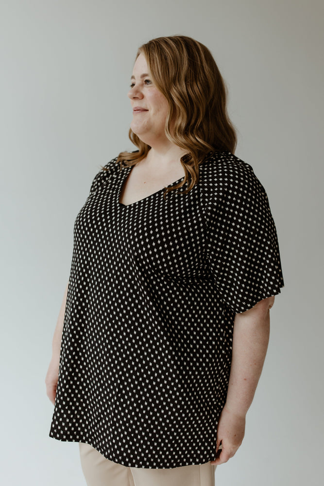 Dressed in Yesta's Breezy Abstract Dot Blouse, a woman with long hair stands out against the plain background as the black and white pattern captivates. The wrinkle-free material enhances the elegance of her stylish appearance.