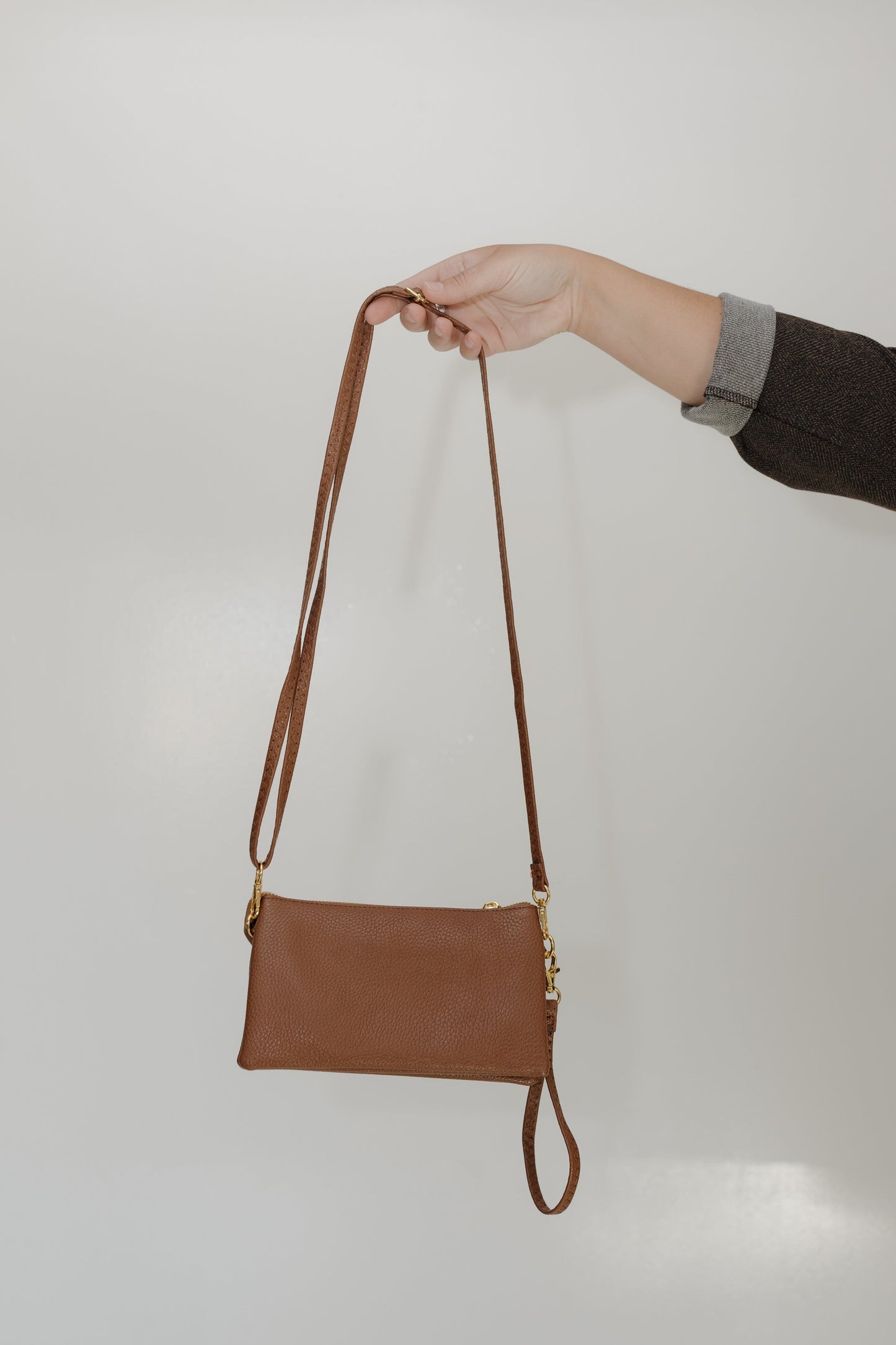 Brown leather crossbody bag held by a hand against a plain background