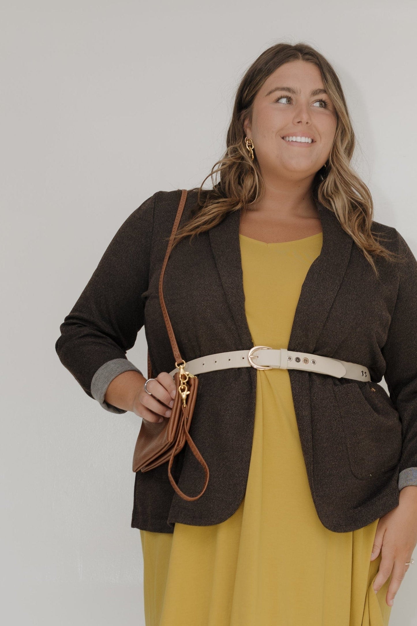 Woman wearing a yellow dress with a brown jacket against a white background